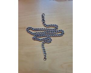 Stainless steel chain necklace on a table. Chain links are medium size. Necklace laid in a vertical heartbeat symbol. 